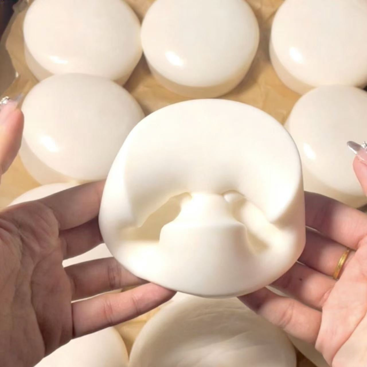Close-up of hands holding a white Yogurt Squishy with a central hole, surrounded by more white ceramic items.