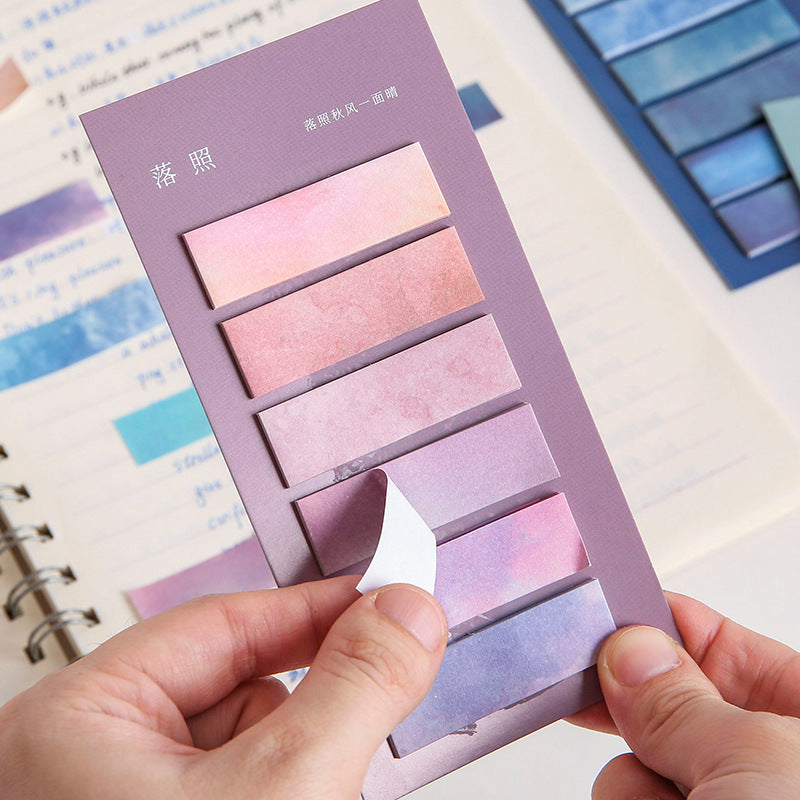 Purple sticky note set with gradient colors held by a hand, blurred background