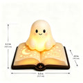 A cute ghost-shaped night light sitting on an open glowing book, shown with dimension arrows and labels indicating height and width on a plain white background.