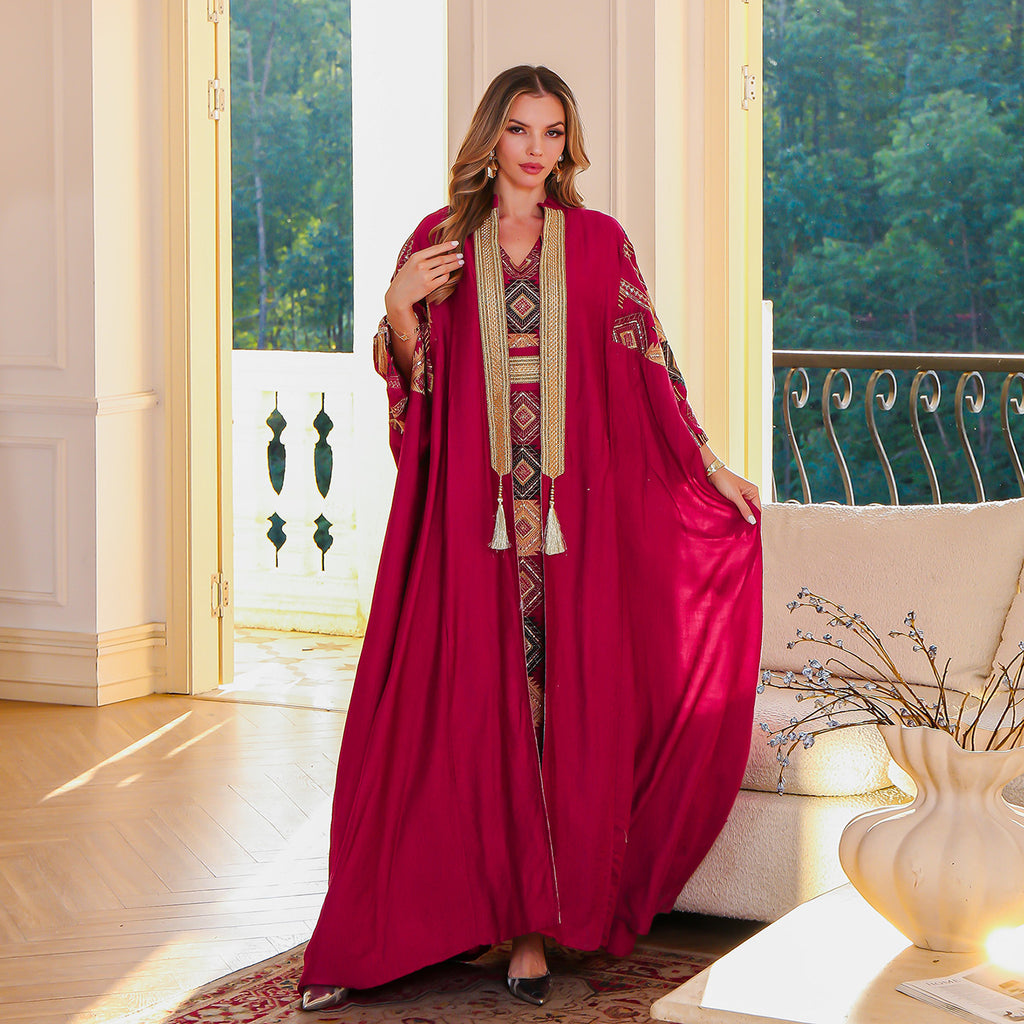 Woman in a red dress with intricate patterns standing in a well-lit room with large windows.
