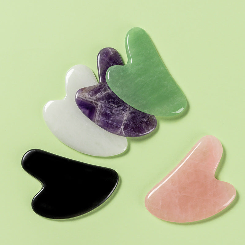 Five gua sha tools in different colors on a light green background