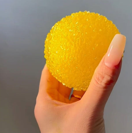 Hand holding a yellow textured ball Squishy against a gray background