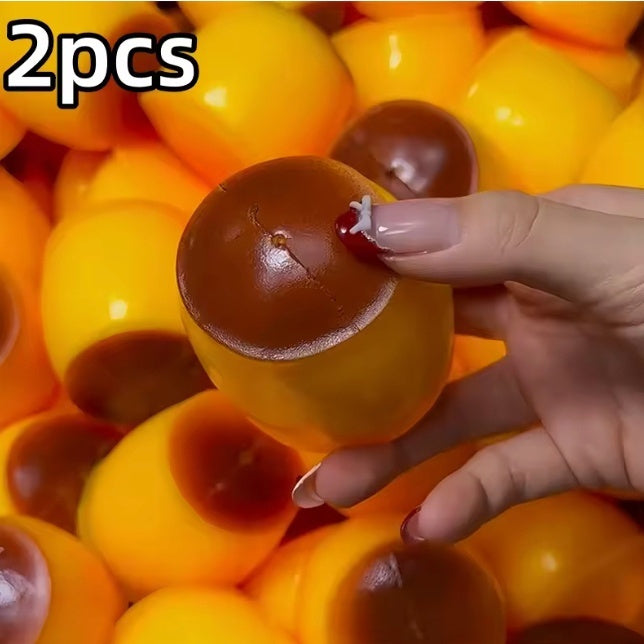 A hand holds a yellow and brown acorn-shaped squishy toy, with a pile of similar yellow and brown acorn-shaped squishy toys in the background. The text '2pcs' is displayed in the top-left corner.
