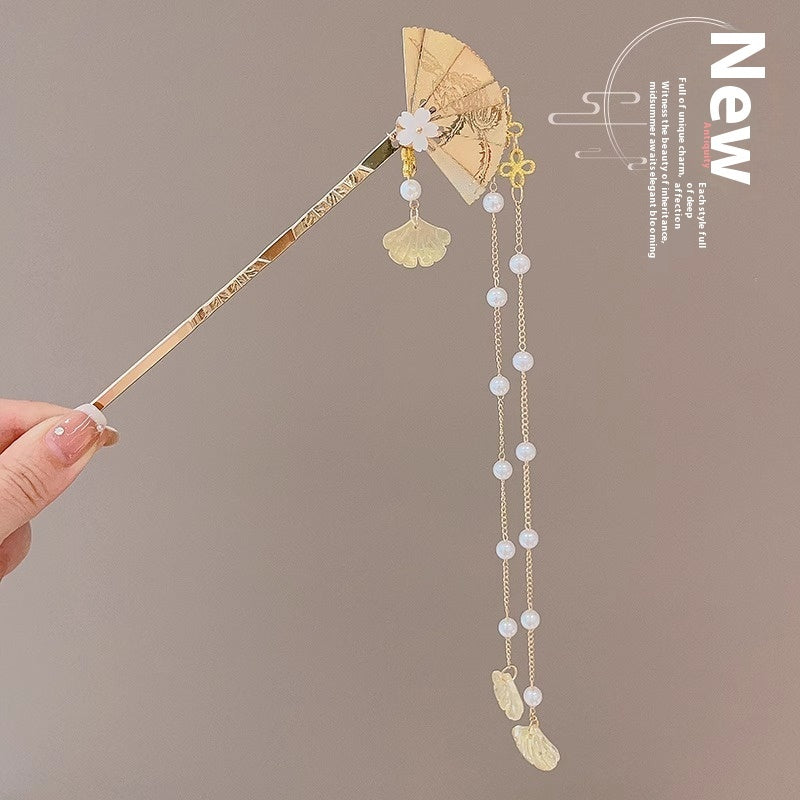 Decorative hairpin with gold and pearl details held by a hand against a brown background