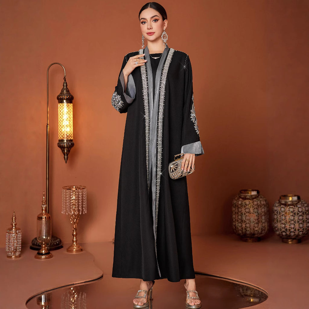 Woman in a black abaya with silver details standing in a decorated room with lamps and vases.