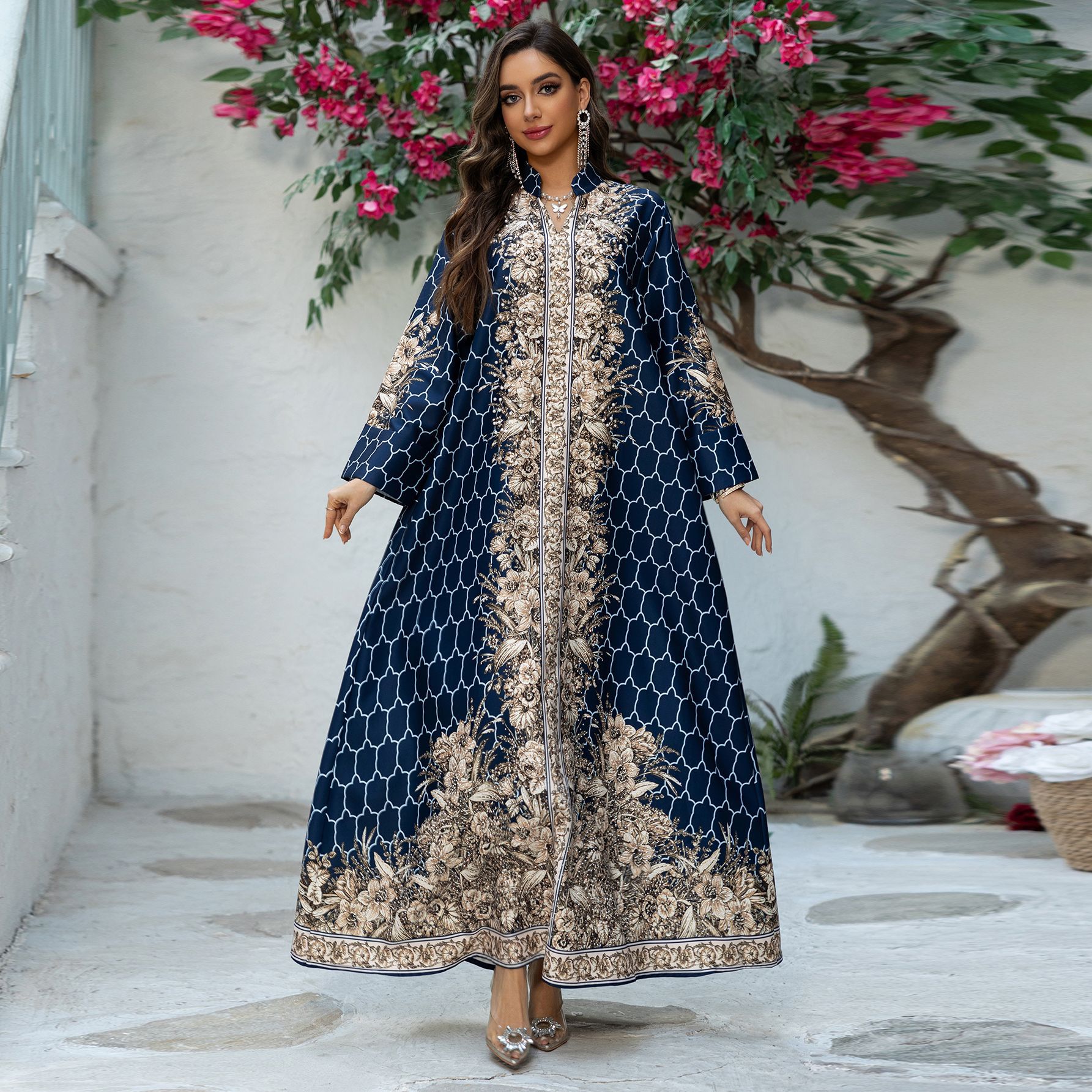 Woman in a blue and gold embroidered dress standing in front of a floral arrangement.
