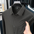 Black and white striped shirt on a hanger with a hand holding it, against a blurred indoor background.
