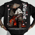 A black short-sleeve t-shirt featuring a large, detailed Japanese samurai graphic on the back. The graphic depicts a samurai in a conical hat with a sword hilt, white and gray armor, and a red sash, surrounded by pink cherry blossoms and Japanese calligraphy.