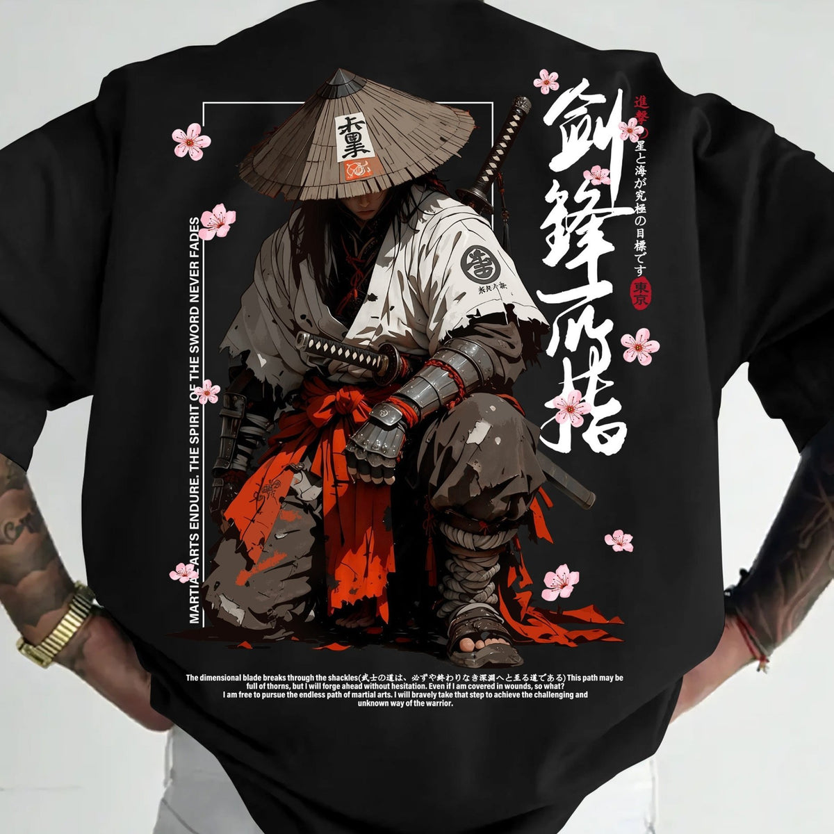 A black short-sleeve t-shirt featuring a large, detailed Japanese samurai graphic on the back. The graphic depicts a samurai in a conical hat with a sword hilt, white and gray armor, and a red sash, surrounded by pink cherry blossoms and Japanese calligraphy.