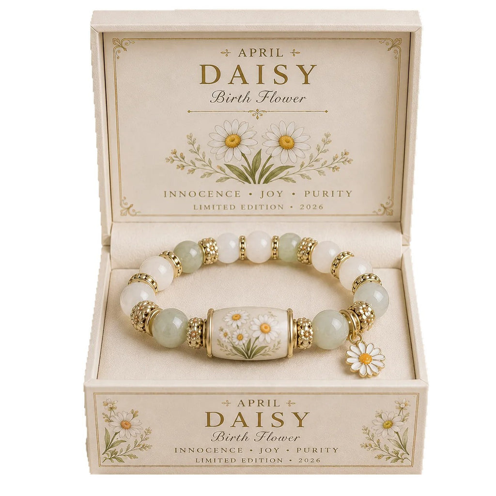 A beaded bracelet with white and pale green beads, gold-toned spacer details, and a central floral charm, presented inside a cream-colored gift box labeled April Daisy Birth Flower.