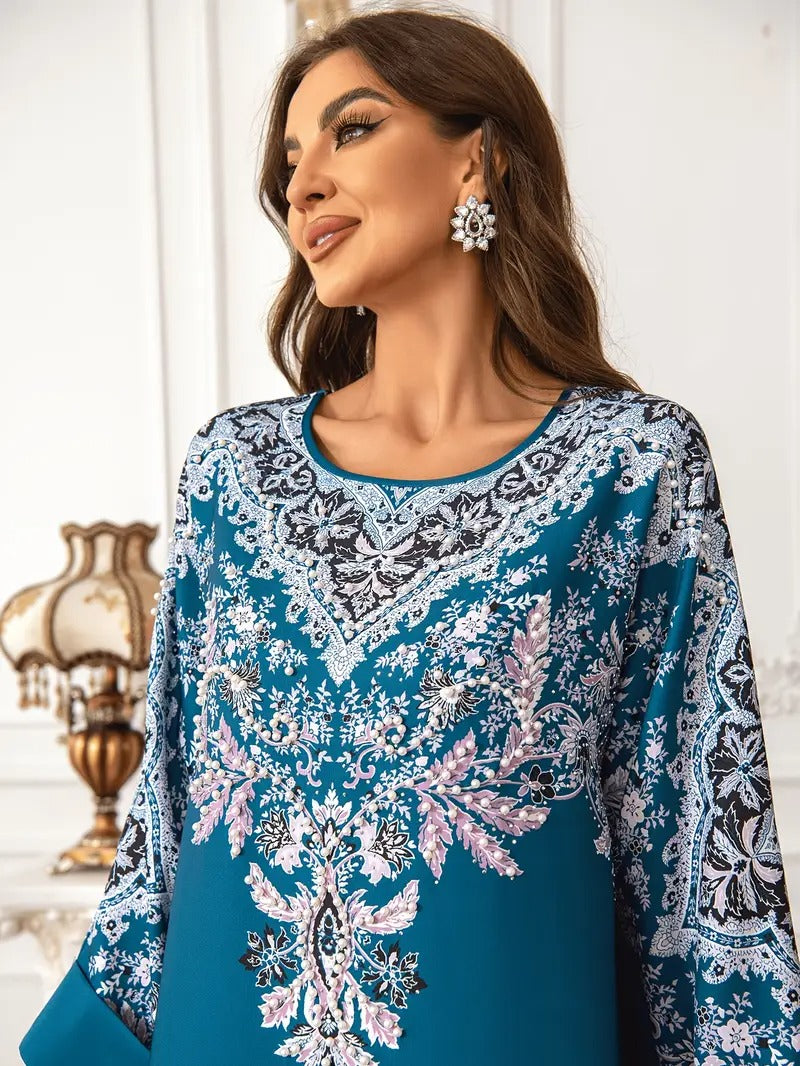 A woman wearing a teal blue embroidered kurta with intricate white, black, and pink floral patterns, styled with matching statement earrings in an elegant indoor setting.