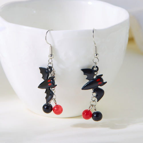 Pair of bat-shaped earrings with red and black beads on a white cup background