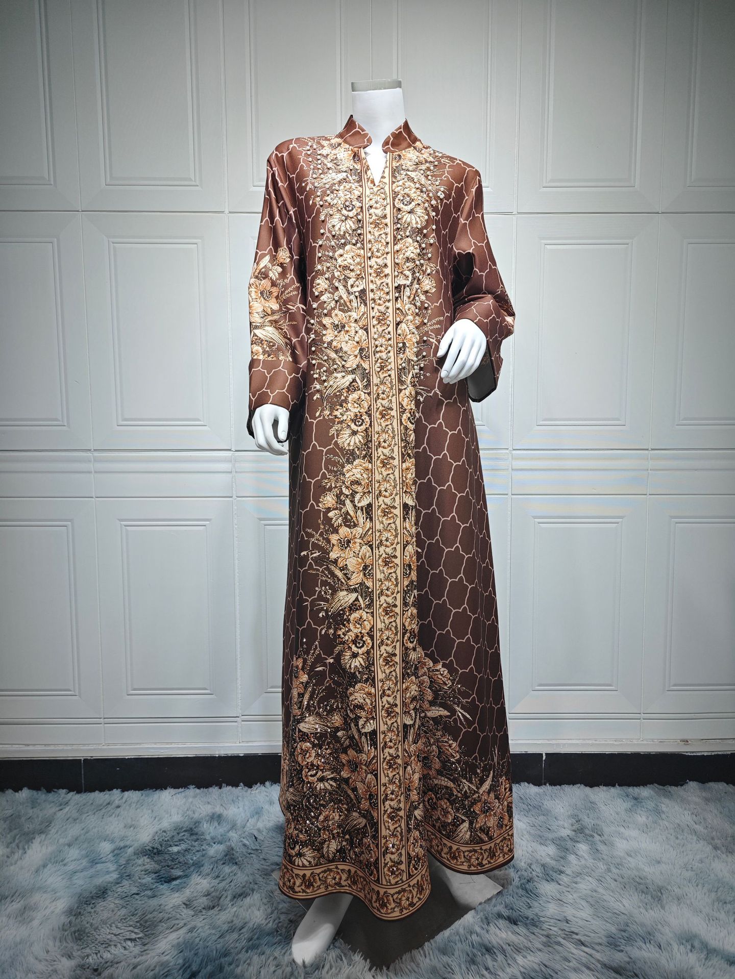 Long brown dress with gold patterns on a mannequin against a white paneled wall.