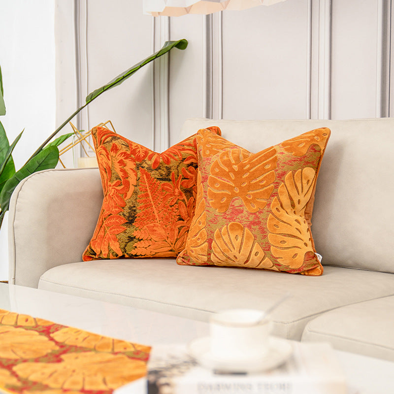 Two decorative throw pillows with orange and yellow botanical leaf patterns resting on a light beige sofa in a styled living room setting.