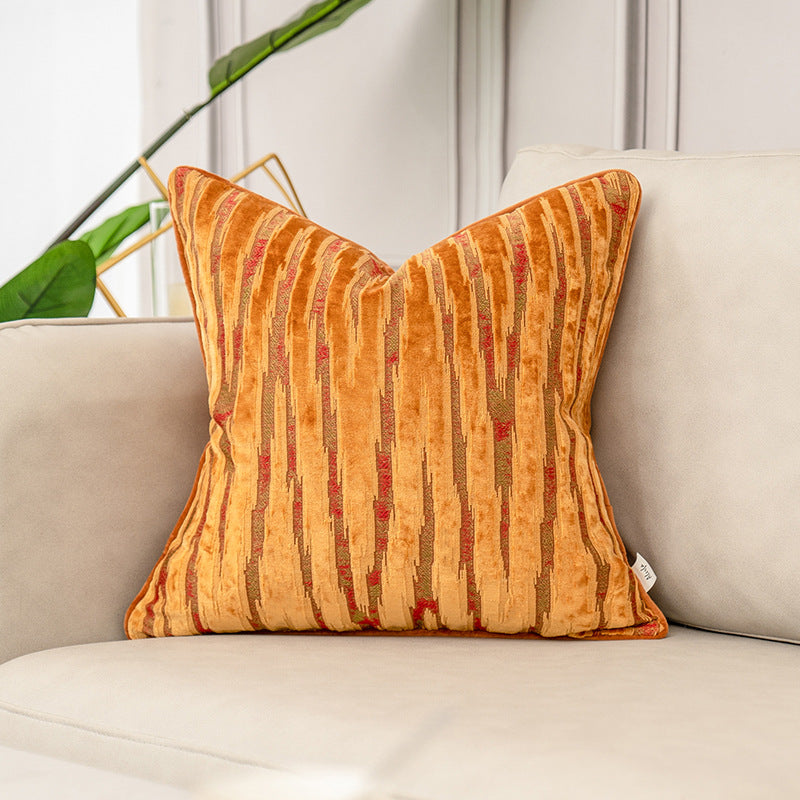 Orange striped pillow on a beige sofa with a plant in the background