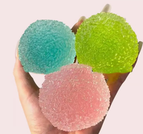Three colorful ball Squishy held in a hand against a light pink background