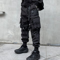 Person wearing black tactical pants and boots against a gray wall.