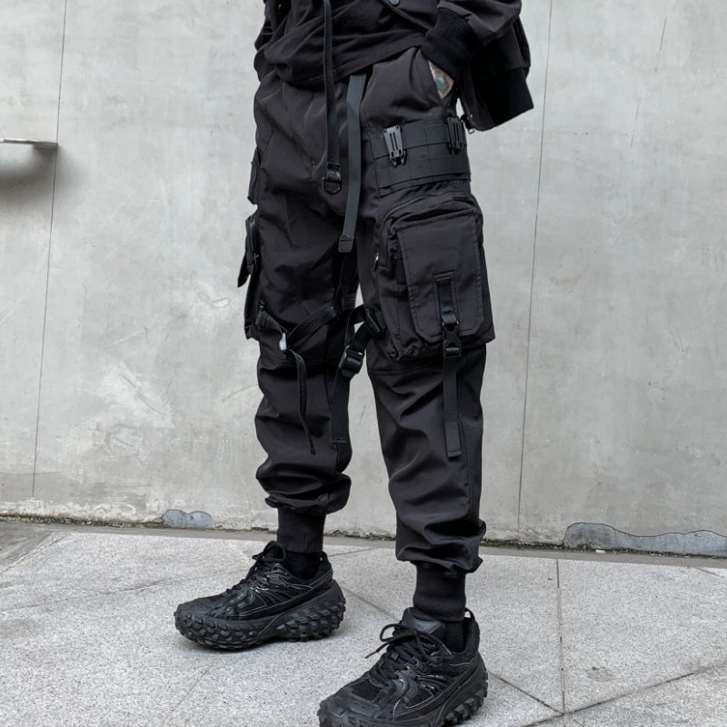 Person wearing black tactical pants and boots against a gray wall.
