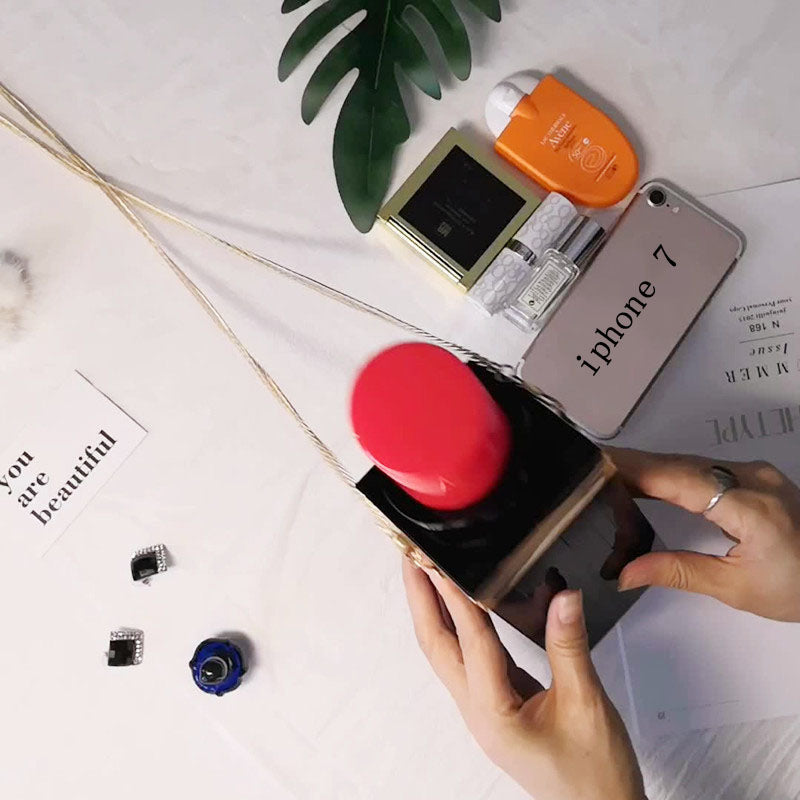 Person opening a black box with a red lid on a white surface with a phone and other items.