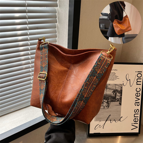 Brown leather handbag with patterned strap on a surface near a window.