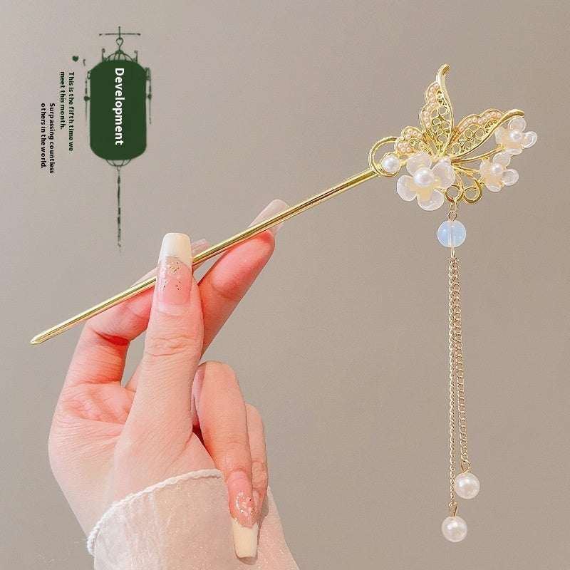 Hand holding a decorative hairpin with pearls and gold elements against a neutral background
