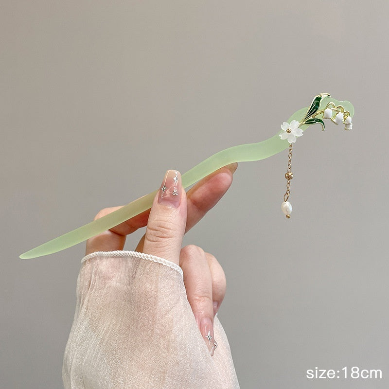 Hand holding a decorative hairpin with flowers against a neutral background
