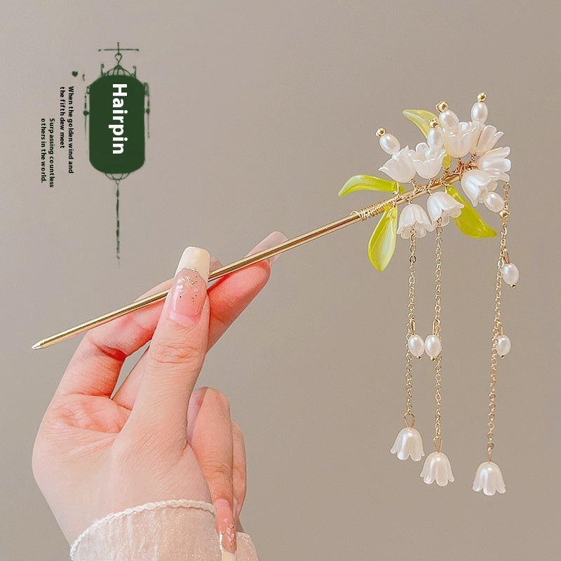 Hairpin with floral design and pearl-like beads held by a hand against a neutral background