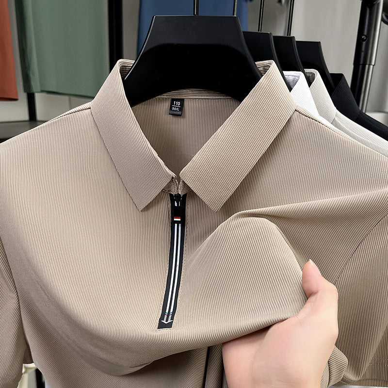 Beige shirt with a zipper held by a hand, with other shirts in the background.