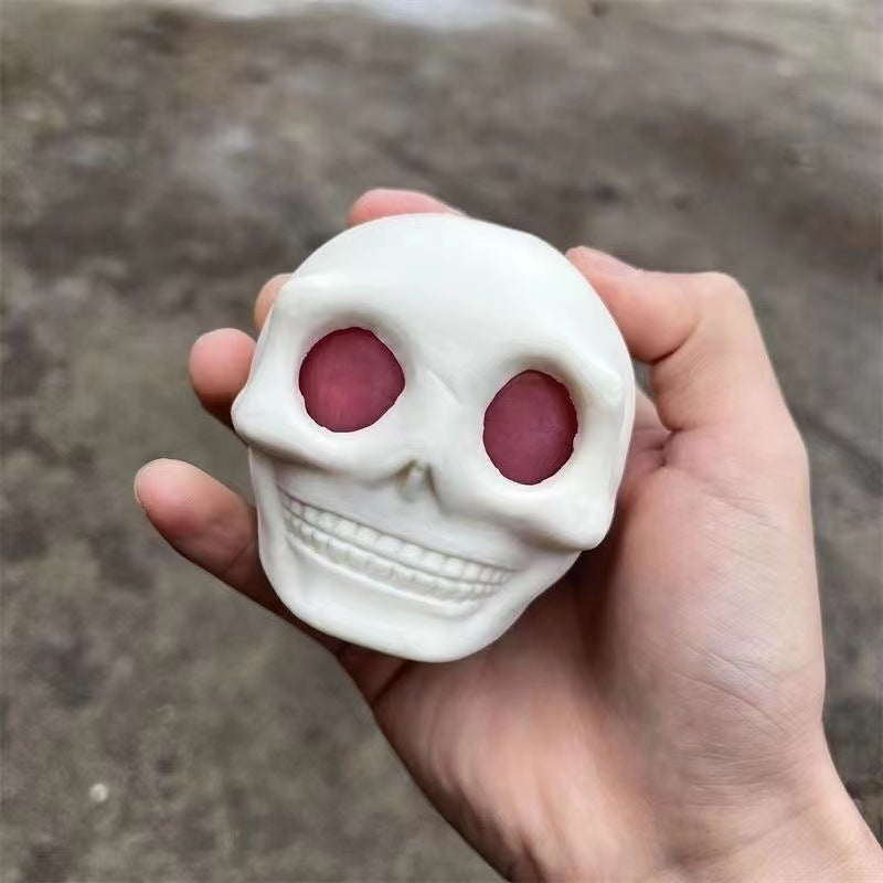 Hand holding a small white skull fidget toy squishy stress relief with pink eyes against a blurred background