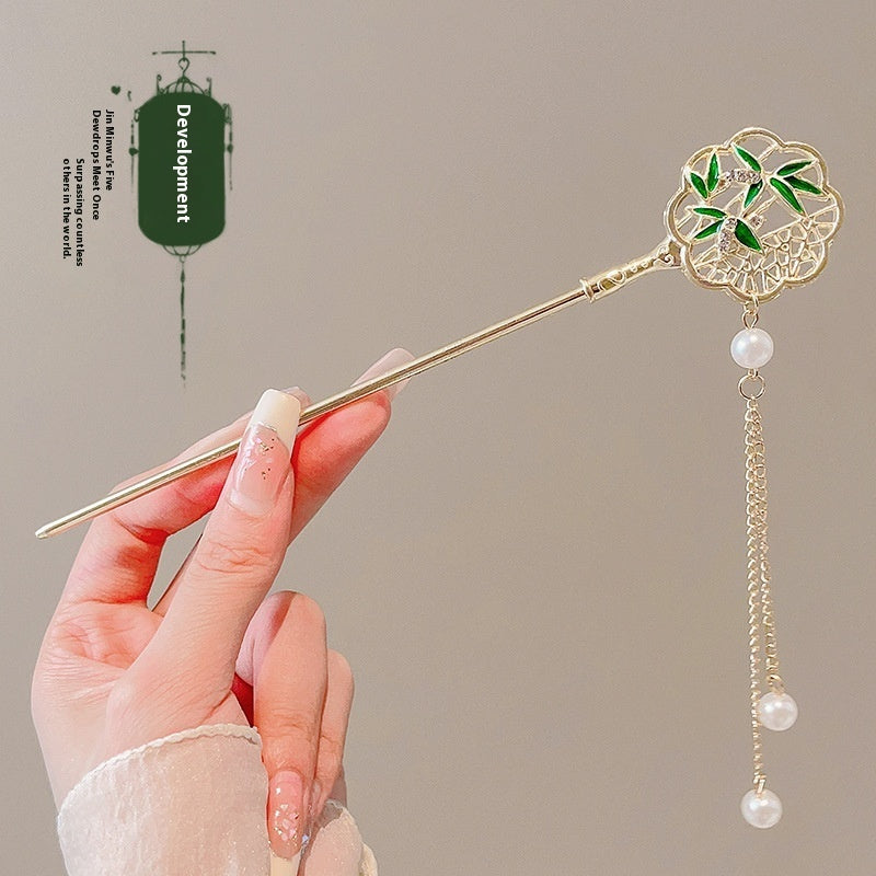 Hand holding a decorative hairpin with green leaves and pearl beads against a beige background