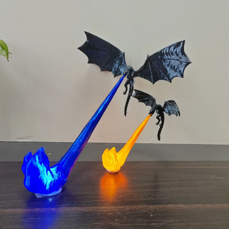 Two black dragon figurines with spread wings, each mounted on a flame-shaped base that glows blue or orange, displayed on a dark wooden surface against a plain beige wall.