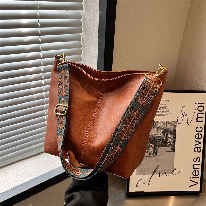 Brown leather handbag with decorative strap against a window and wall.
