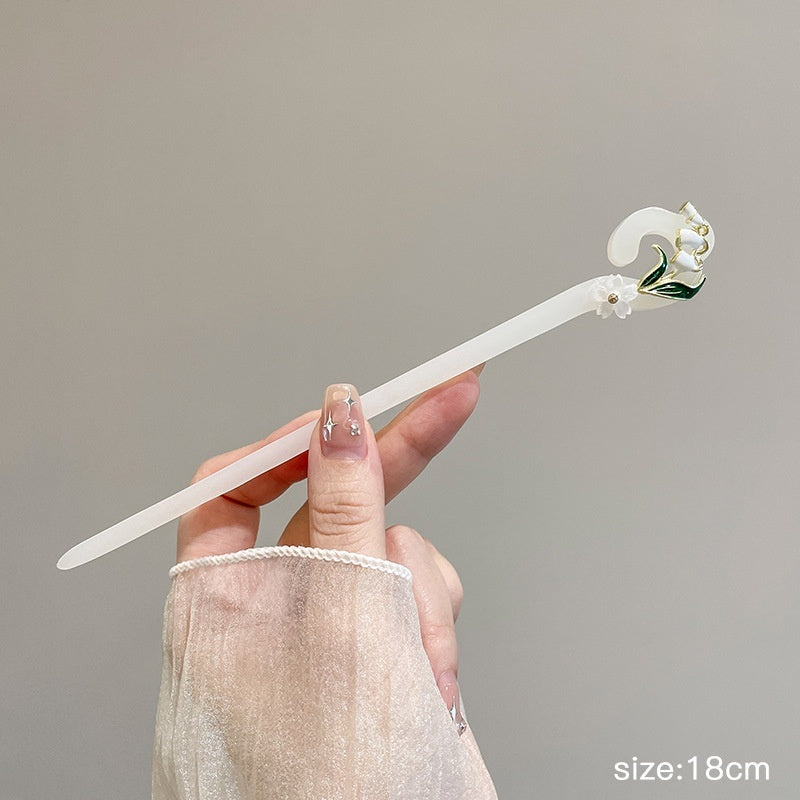 Decorative hairpin held by a hand against a neutral background