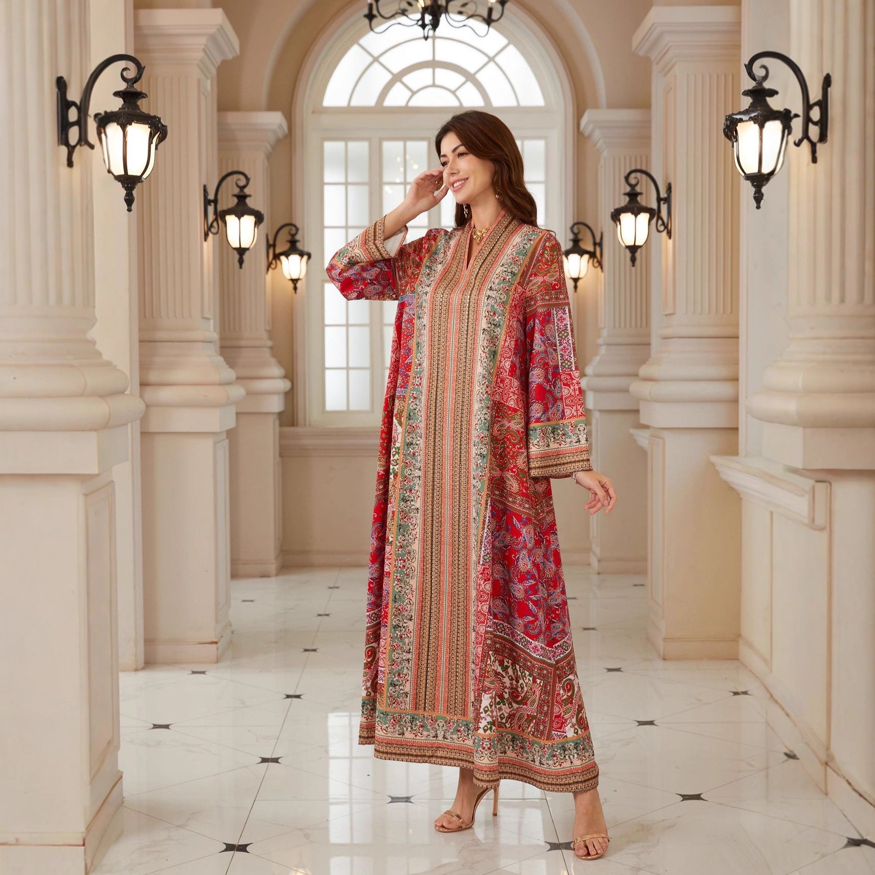 Woman in a red and gold traditional outfit standing in an elegant hallway with columns and lights.