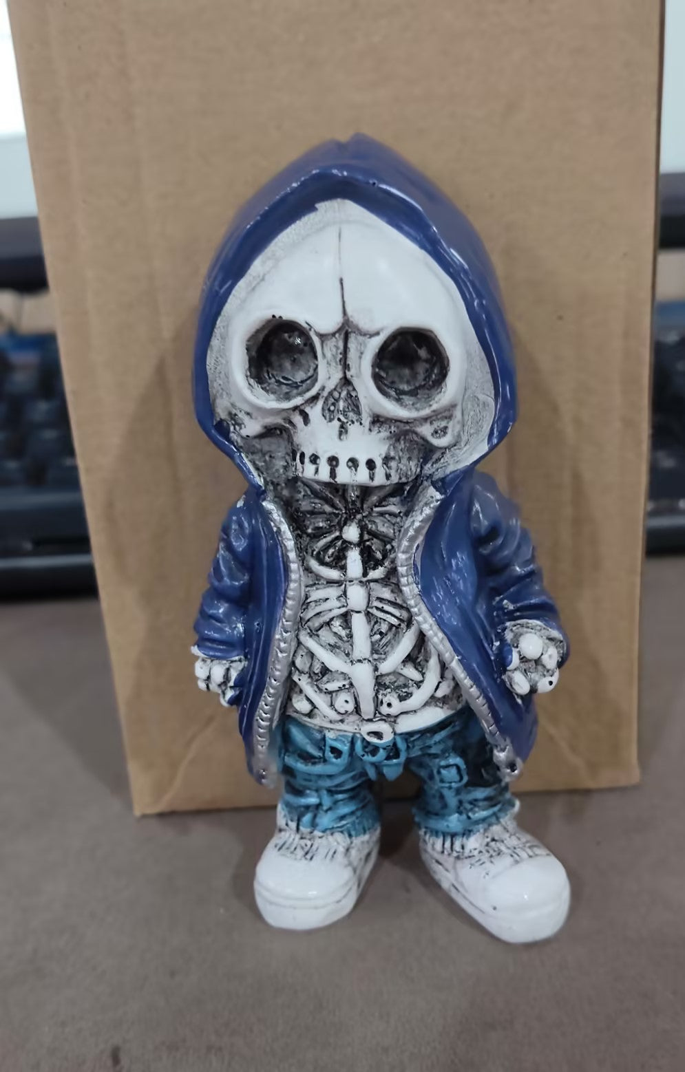 Skeleton figure in a blue hoodie and jeans standing against a cardboard background