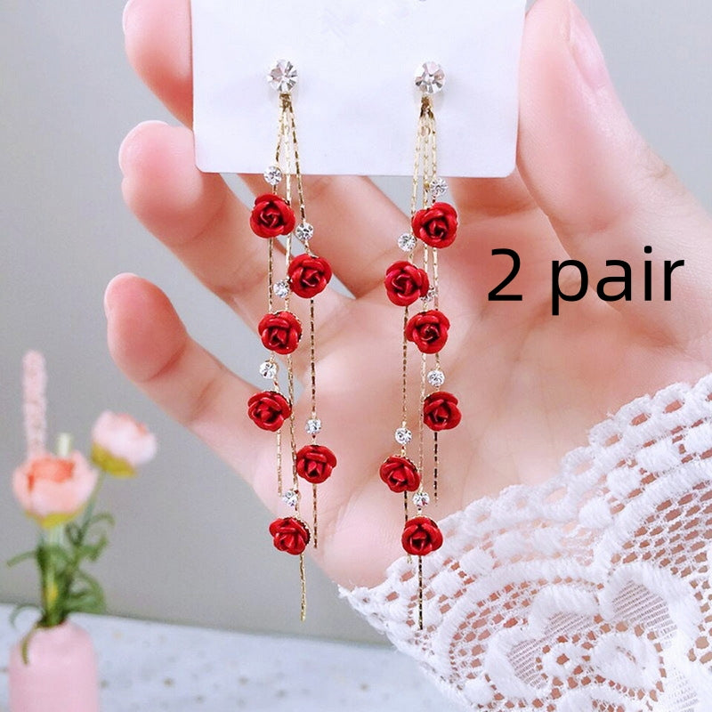 Red rose earrings held by a hand with a blurred background