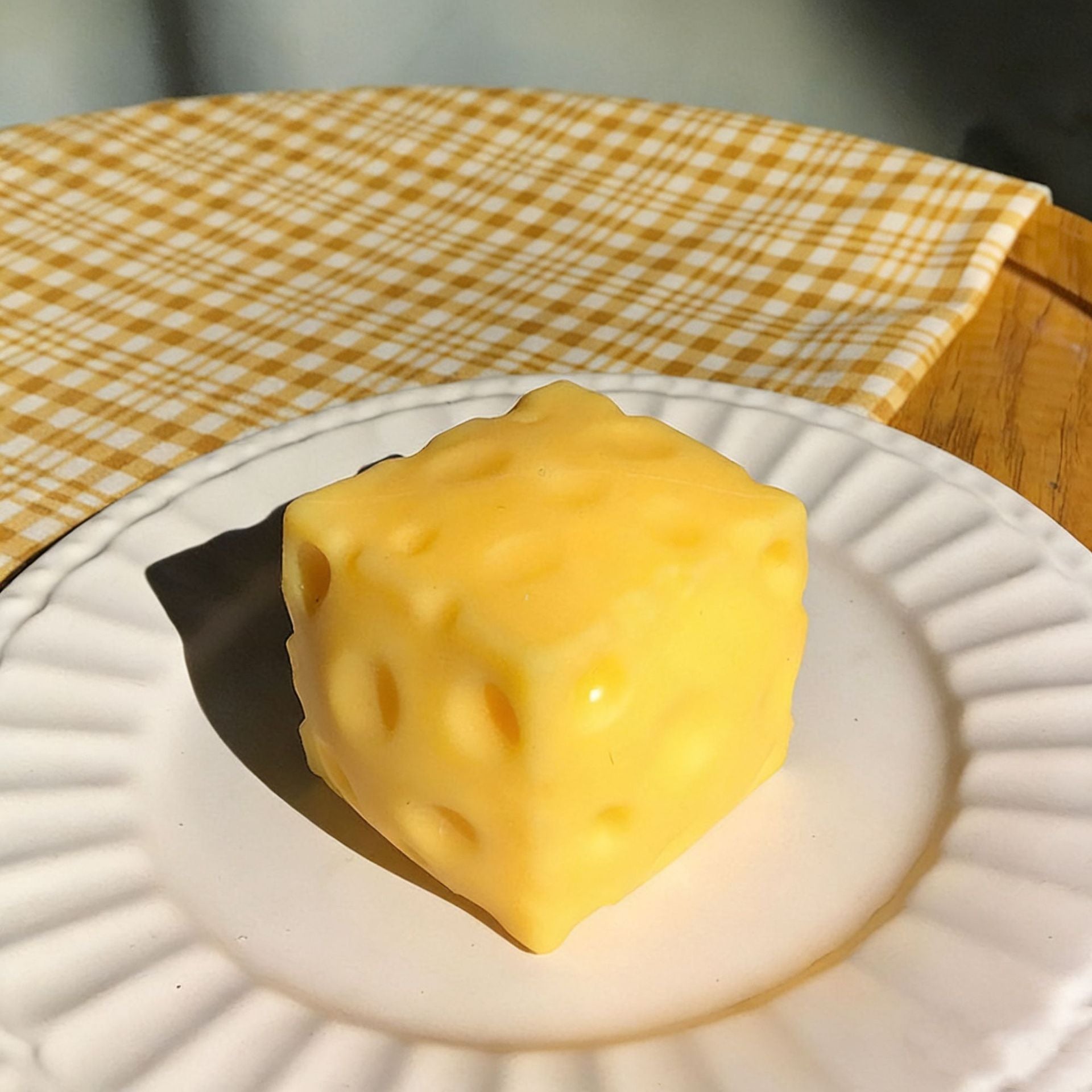 Yellow cheese cube squishy on a white plate with a checkered tablecloth in the background