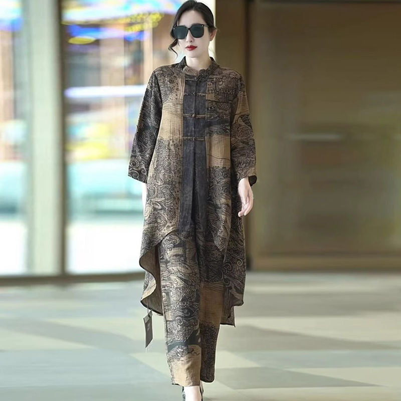A woman wearing a long-sleeved, high-low, patchwork-style dress with a dark brown and beige abstract landscape print, walking in a modern indoor setting.