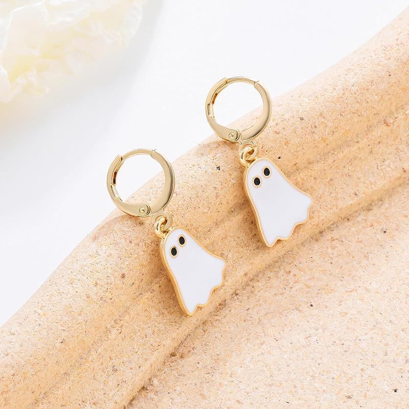 Gold hoop earrings with ghost charms on a beige surface