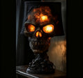A gothic skull table lamp with a black fabric shade, featuring a detailed skull sculpture with glowing orange light inside its eye sockets and cracked bone texture on the crown, set on a dark wooden surface.
