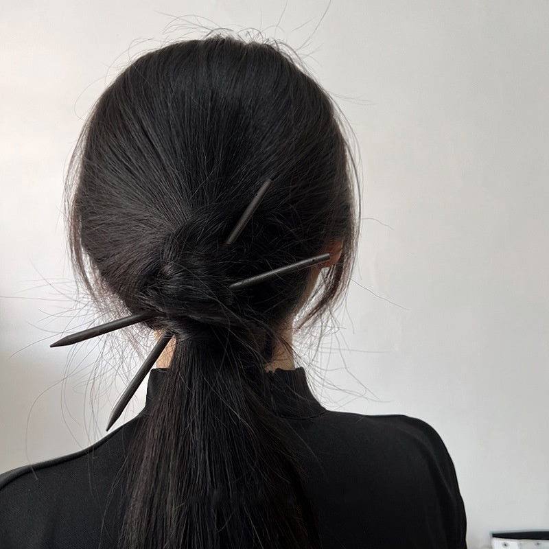 Person with black hair styled in a ponytail with decorative hairpins against a white background