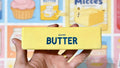 Hand holding a yellow phone case with 'Salted Butter squishy' text against a colorful background