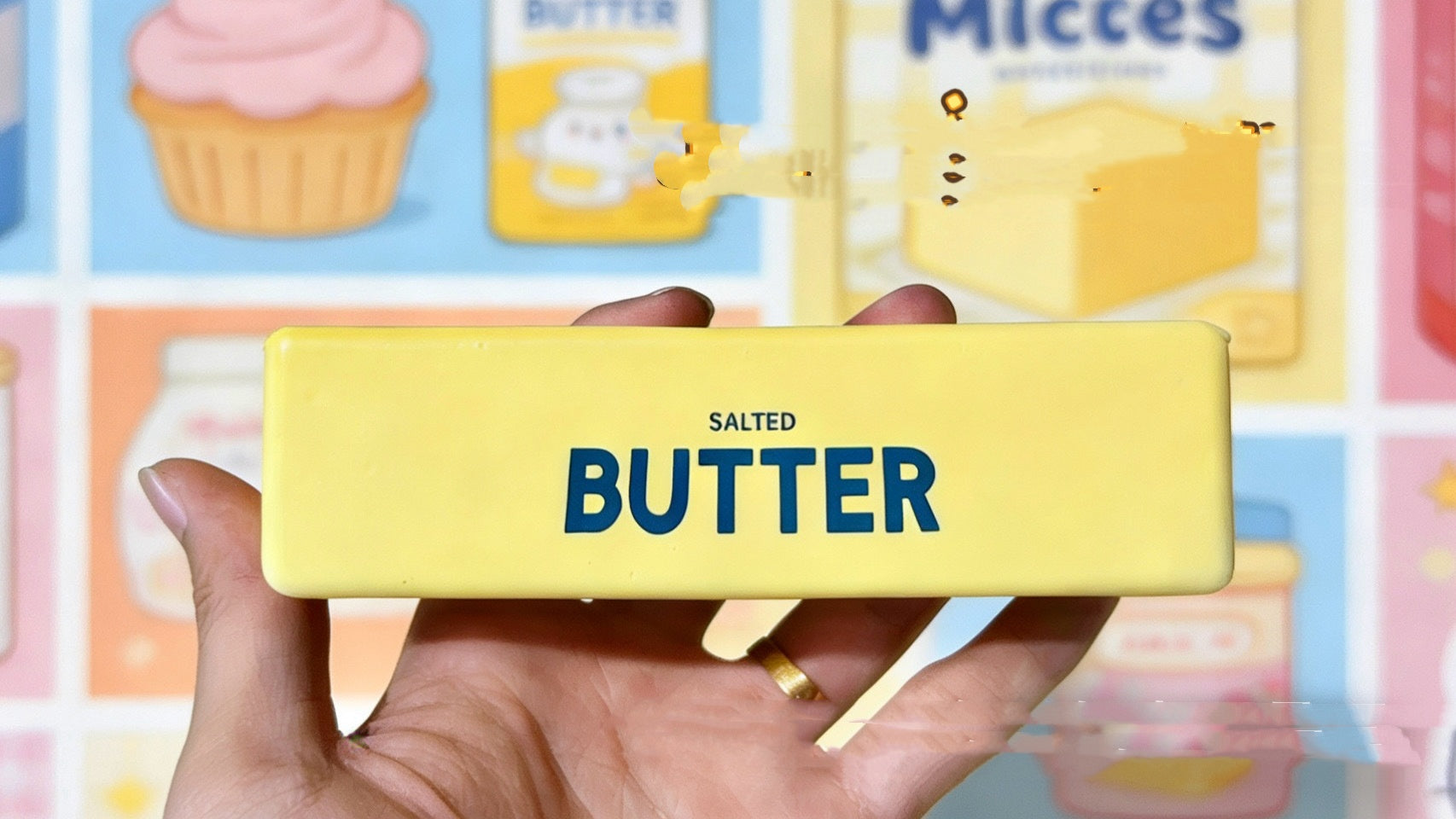 Hand holding a yellow phone case with 'Salted Butter squishy' text against a colorful background
