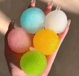 Hand holding colorful, glittery balls Squishy against a neutral background