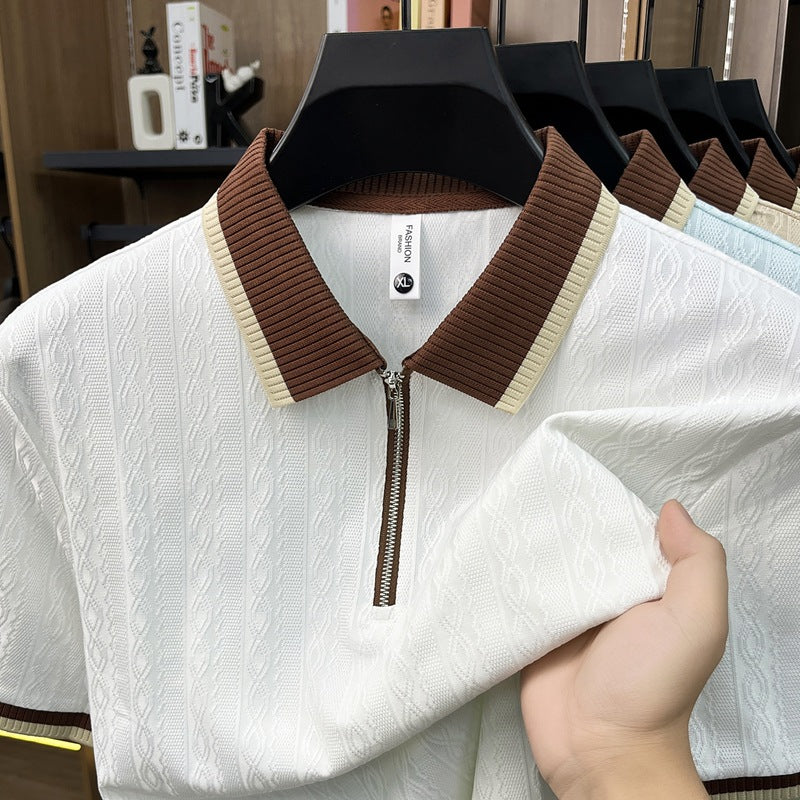 White sweater with brown collar held by a hand, with more sweaters in the background.