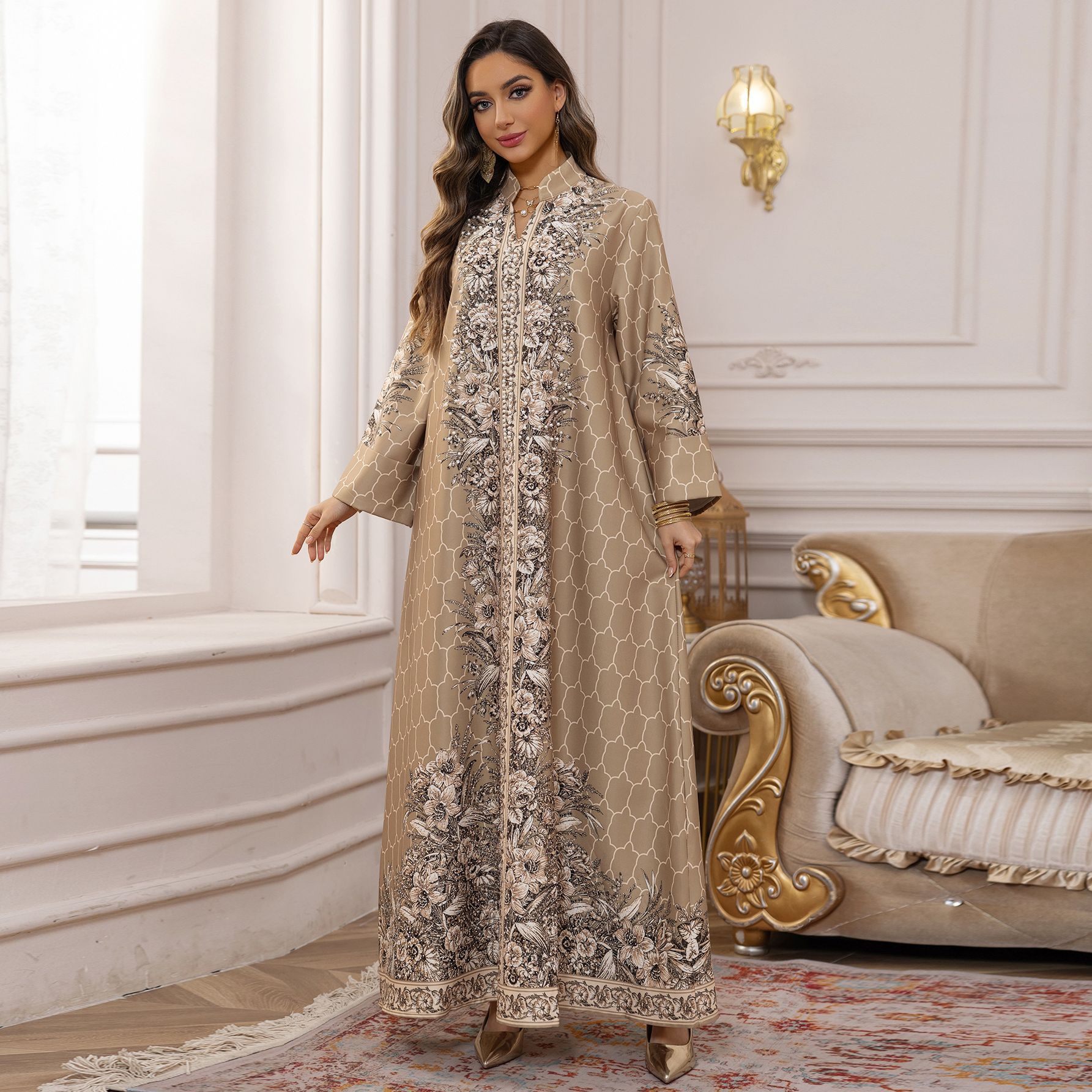 Woman in a beige embroidered dress standing in an elegant room with a sofa and lamp.