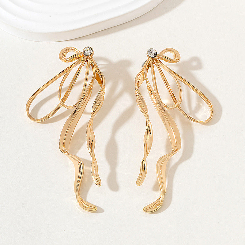 Gold earrings with a bow design on a light background