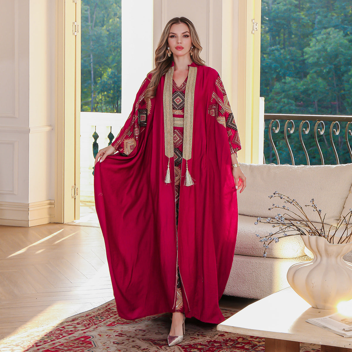 Woman in a red abaya with intricate patterns standing in a well-lit room.