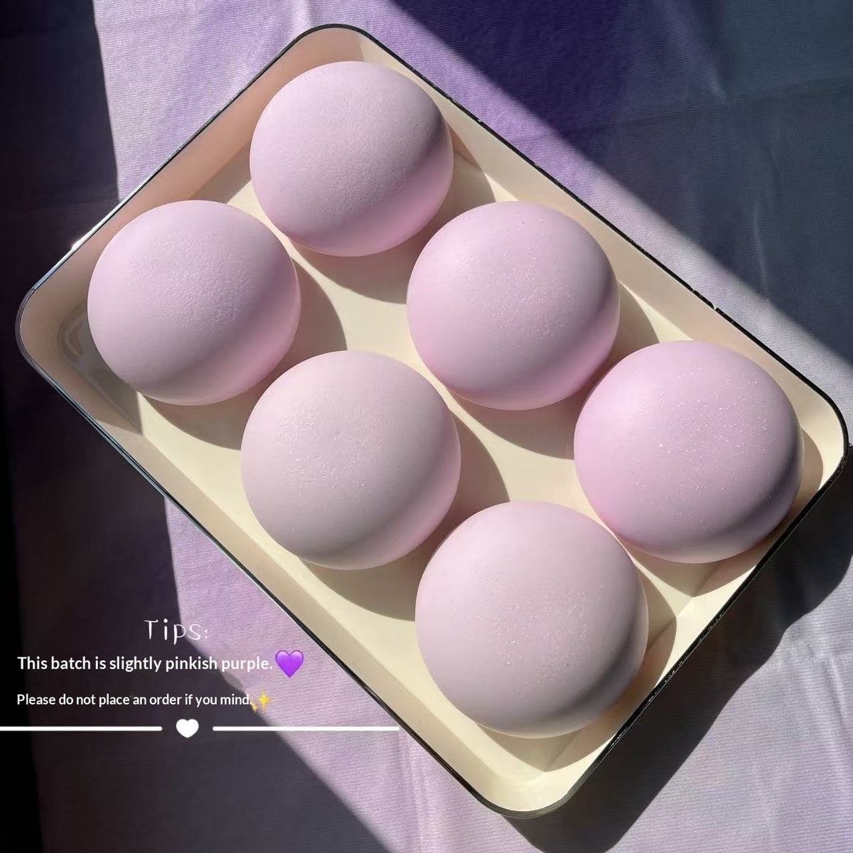 Set of pink makeup sponges in a tray on a purple fabric background