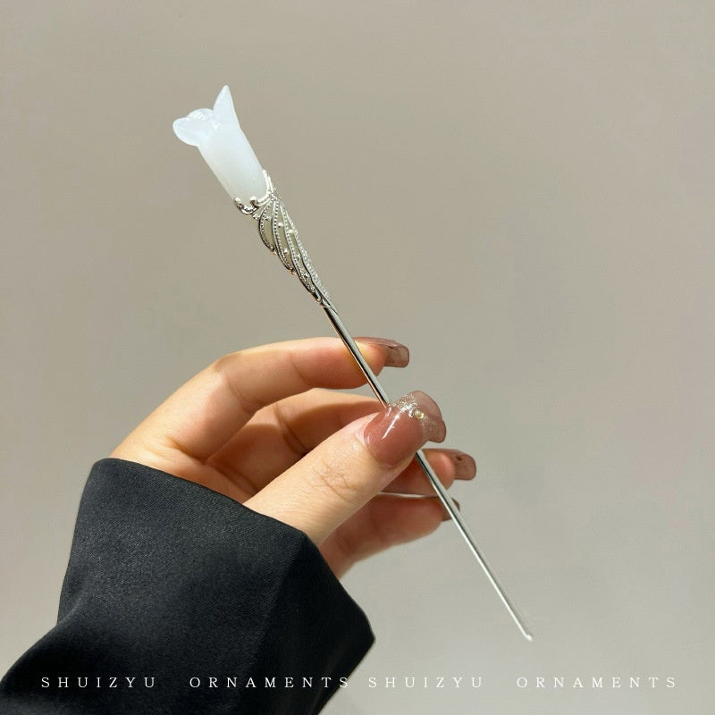 Hand holding a decorative hairpin with a white stone and silver design against a neutral background.